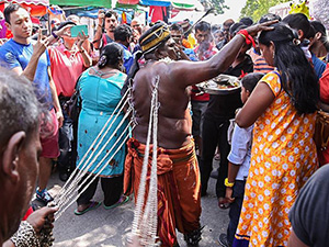 Photo of a man with his back pierced with hooks which are attached to the chains pulled by another man, resembling a horse pulling the carriage - the man is giving blessings to other pilgrims at Thaipusam 2017, photo by Ivan Kralj