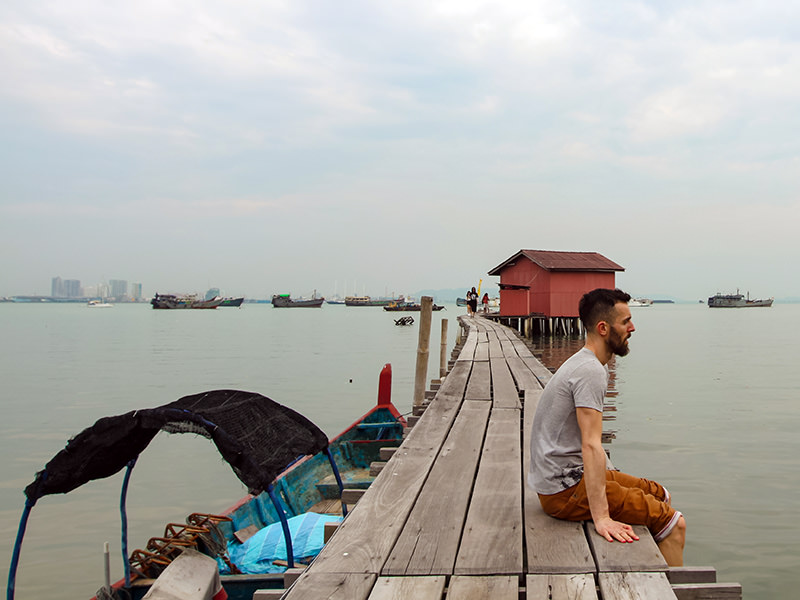 Pipeaway blogger Ivan Kralj sitting on one of the jetties in Georgetown, Penang Island, Malaysia, boats lining up on the horizon, photo by Weile Ng