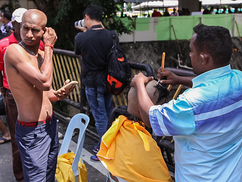 Photograph of a street barber shaving bald one of the Thaipusam pilgrims, photo by Ivan Kralj