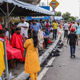 Photograph of street barbers shaving thhe heads of Thaipusam pilgrims, covering the streets in hair, photo by Ivan Kralj