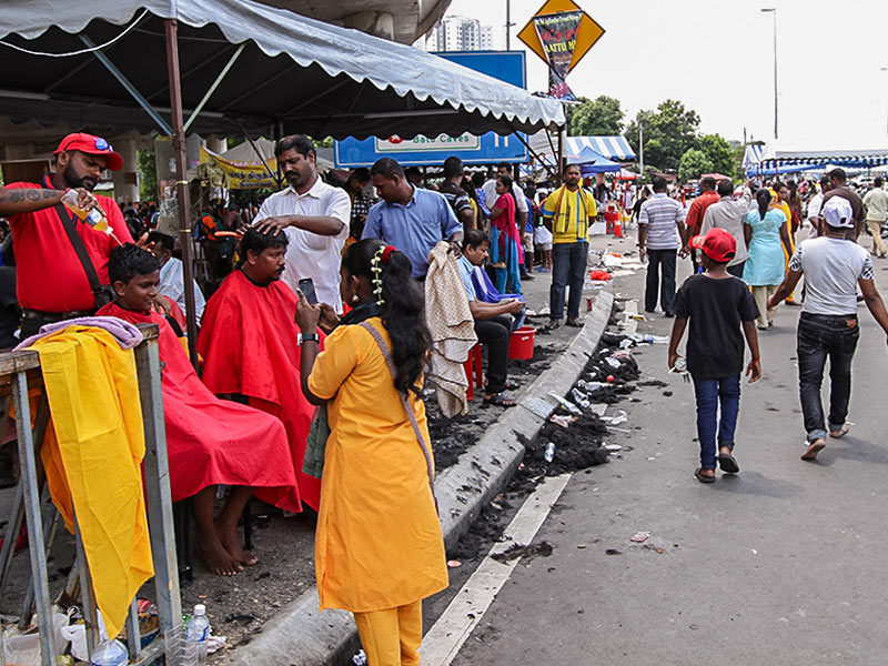 Photograph of street barbers shaving thhe heads of Thaipusam pilgrims, covering the streets in hair, photo by Ivan Kralj