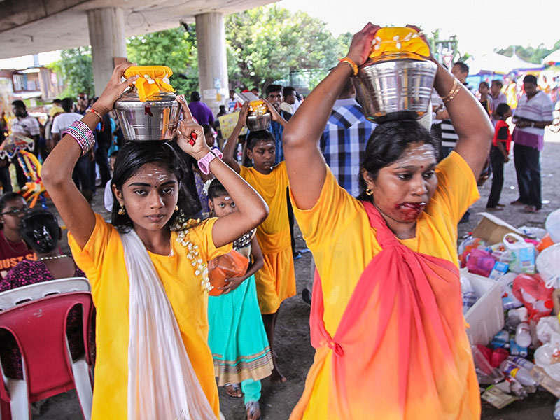 Photograph of a woman and her daughters carrying Paal Kudam milk pots on their heads, the woman's mouth are bleeding from the piercing ritual, photo by Ivan Kralj