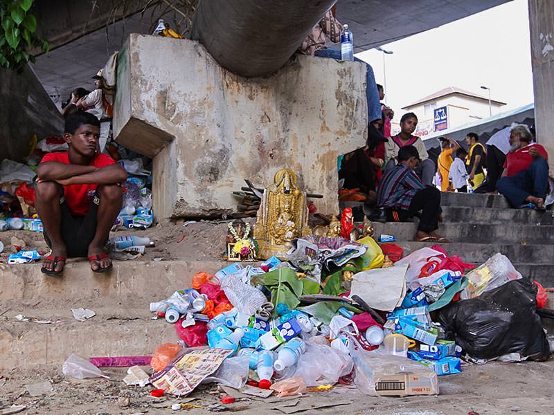 Photograph of a boy sitting next to a pile of garbage with some altar elements such as sculptures of deities, photo by Ivan Kralj