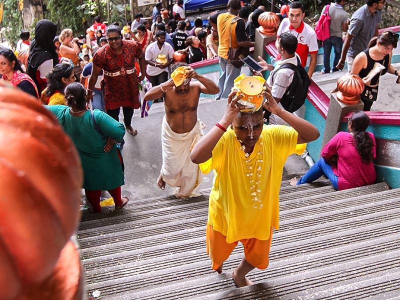 Photograph of pilgrims carrying Paal Kudam, brass pots filled with milk, as offerings for Thaipusam festival, the boy climbing the stairs to Batu Caves is spilling the milk all over his face, photo by Ivan Kralj