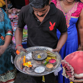 A man in a black T-shirt, with the red logo of Playboy magazine, holding a plate with sacred ashes ath Thaipusam festival, photo by Ivan Kralj