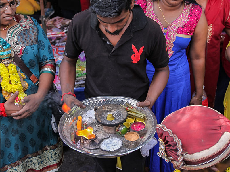 A man in a black T-shirt, with the red logo of Playboy magazine, holding a plate with sacred ashes ath Thaipusam festival, photo by Ivan Kralj