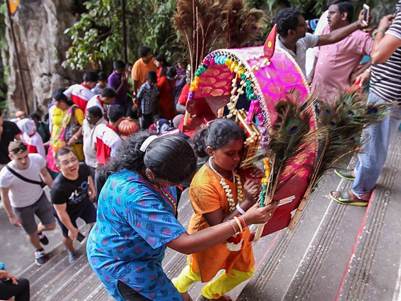 Photograph of a mother helping her young daughter carrying a heavy Kavadi altar while climbing the stairs of Batu Caves for Thaipusam festival, photo by Ivan Kralj