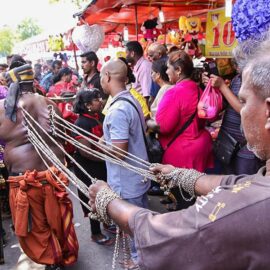Photograph of a man pulling the chains attached to the hooks piercing the skin of the back of the other man, an extreme ritual at Thaipusam festival, photo by Ivan Kralj