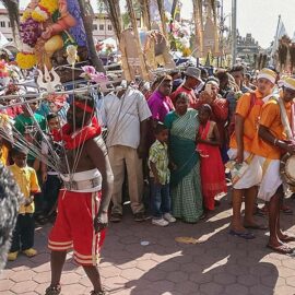 Photograph of a Thaipusam pilgrim dancing while carrying a Kavadi, a portable altar at Thaipusam, while the crowds observe - the structure is worn on his shoulders while the skewers are pressing the bearer's torso, photo by Ivan Kralj