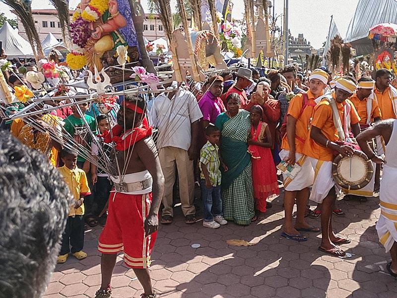 Photograph of a Thaipusam pilgrim dancing while carrying a Kavadi, a portable altar at Thaipusam, while the crowds observe - the structure is worn on his shoulders while the skewers are pressing the bearer's torso, photo by Ivan Kralj