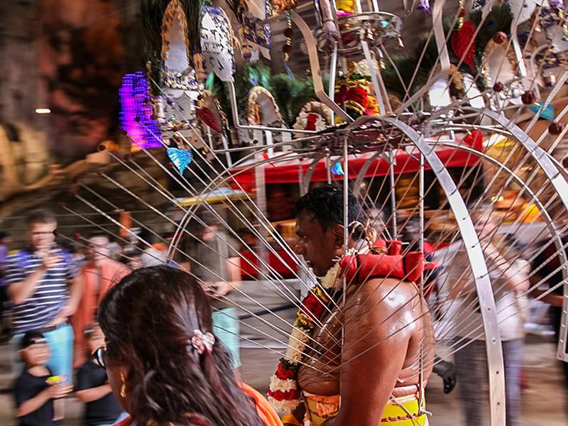 Photograph of a Thaipusam pilgrim carrying a Kavadi, a portable altar at Thaipusam - the structure is worn on his shoulders while the skewers are pressing the bearer's torso. Pilgrim is entering Batu Caves, photo by Ivan Kralj