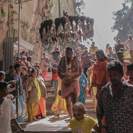 Photograph of a Thaipusam pilgrim carrying a Kavadi, a portable altar at Thaipusam - the structure is worn on his shoulders while the skewers are pressing the bearer's torso. Pilgrim is entering Batu Caves, while the crowds observe, photo by Ivan Kralj