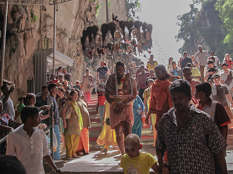 Photograph of a Thaipusam pilgrim carrying a Kavadi, a portable altar at Thaipusam - the structure is worn on his shoulders while the skewers are pressing the bearer's torso. Pilgrim is entering Batu Caves, while the crowds observe, photo by Ivan Kralj