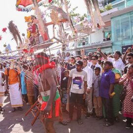 Photograph of a Thaipusam pilgrim dancing while carrying a Kavadi, a portable altar at Thaipusam, while the crowds observe - the structure is worn on his shoulders while the skewers are pressing the bearer's torso, photo by Ivan Kralj