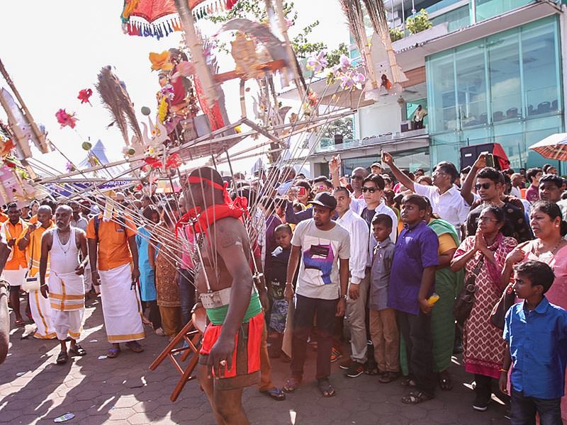 Photograph of a Thaipusam pilgrim dancing while carrying a Kavadi, a portable altar at Thaipusam, while the crowds observe - the structure is worn on his shoulders while the skewers are pressing the bearer's torso, photo by Ivan Kralj