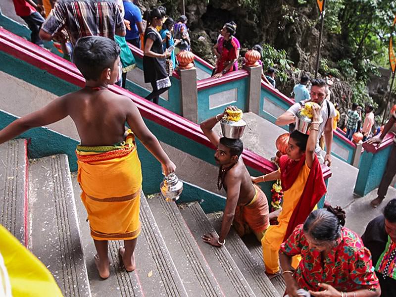 Photograph of a boy at the stairs of Batu Caves, providing space for his father's climb - his father is carrying Paal Kudam, brass pot filled with milk, on his head, while moving on his knees at Thaipusam festival, photo by Ivan Kralj