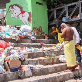 Photograph of a pilgrim praying in front of the improvised altars in piles of trash at the river bank at Thaipusam festival