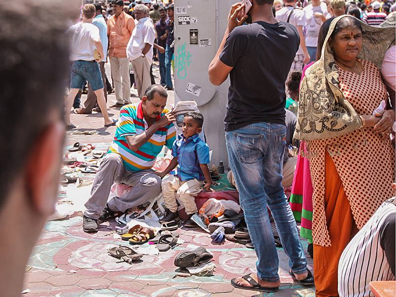 Photograph of a man holding the newspapers in the air to provide a shade for his grandson at Thaipusam festival, photo by Ivan Kralj