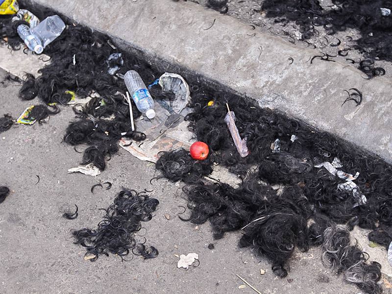 Photograph of a street covered with hair and some garbage, left after the barbers shaved thousands of Thaipusam pilgrims, photo by Ivan Kralj