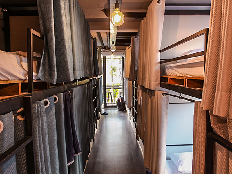 Photo of a dormitory in The Laban hotel, two rows of curtained bunk beds separated by the corridor between them, big lightbulbs, photo by Ivan Kralj