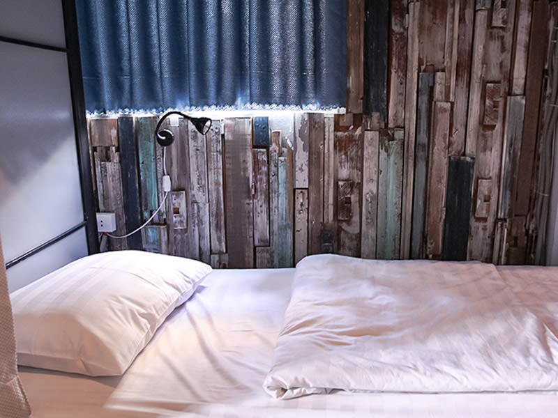 Photo of the bed in the dormitory of The Laban hotel, white bedsheets in front of the blue-grey planks covering the wall, photo by Ivan Kralj