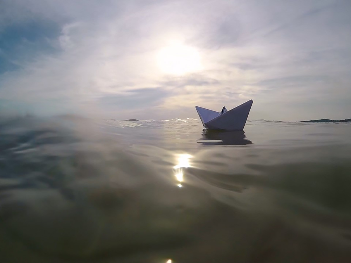 A paper boat floating away in the ocean at sunset in Vietnam; photo by Ivan Kralj.