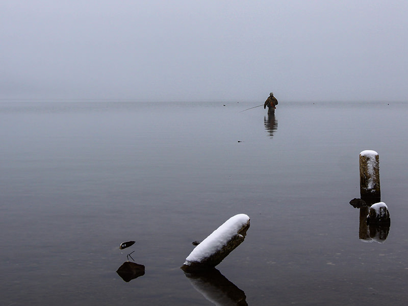 A fisherman standing knee-deep in the snow-surrounded Chuzenji Lake, close to Nikko, Japan, photo by Ivan Kralj