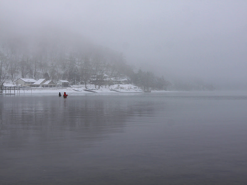 Two fishermen standing waist-deep in the snow-surrounded Chuzenji Lake, close to Nikko, Japan, photo by Ivan Kralj