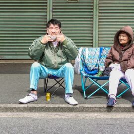 A couple sitting in the chairs in the street, saving their spot for the penis parade at Kanamara Matsuru, festival of the iron penis, in Kawasaki, Japan, photo by Ivan Kralj