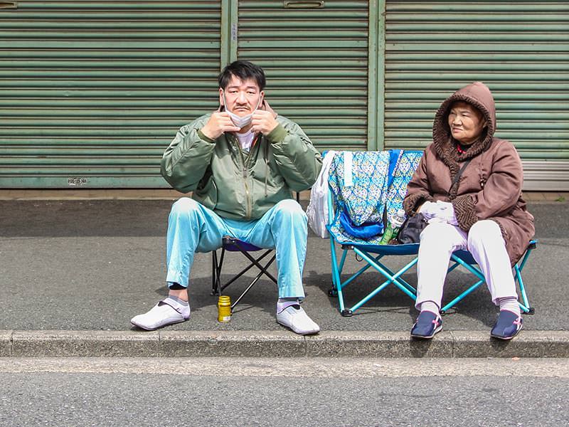 A couple sitting in the chairs in the street, saving their spot for the penis parade at Kanamara Matsuru, festival of the iron penis, in Kawasaki, Japan, photo by Ivan Kralj