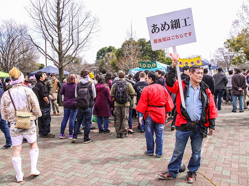 Bored-looking man holding a promo sign for selling lollipops at Kanamara Matsuru, festival of the iron penis, in Kawasaki, Japan, photo by Ivan Kralj