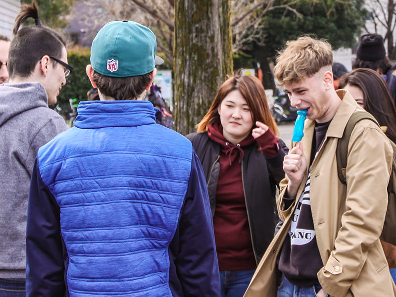 A young guy in a group of friends is licking the penis shaped lollipop at Kanamara Matsuru, festival of the iron penis, in Kawasaki, Japan, photo by Ivan Kralj