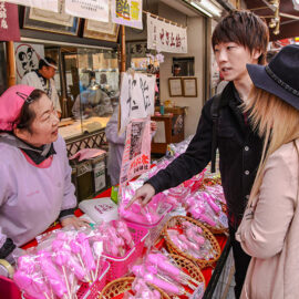 Lady seller and customers at the market discussing the pink candy products she is selling, at Kanamara Matsuru, festival of the iron penis, in Kawasaki, Japan, photo by Ivan Kralj