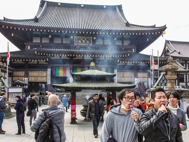 Men licking penis-shaped lollipops in front of the temple in Kawasaki, Japan, during the Kanamara Matsuri, festival of the iron penis, photo by Ivan Kralj