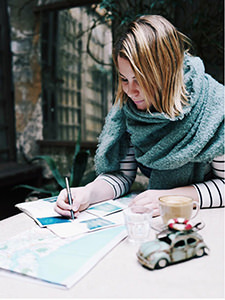 Photographer Kim Leuenberger writing something on the table covered with maps and with a coffee and vintage toy car next to her, photo by Kim Leuenberger