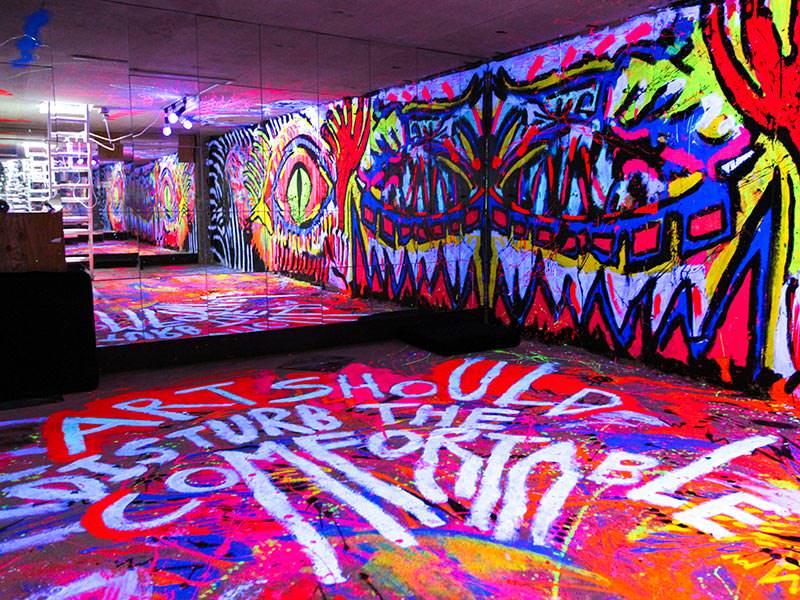 One of the most colorful rooms in hostels in Tokyo, Japan: basement in ARTnSHELTER hostel with walls painted in fluorescent colors, and "Art should disturb the comfortable" message on the floor, by Singaporean street artist Zon, photo by Ivan Kralj