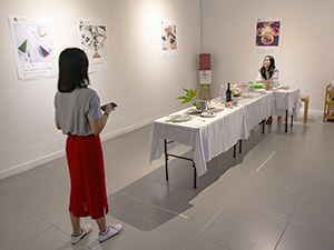 The girl posing for a photograph at the table of Hapsari's artwork "Antara", sitting in the sand as if on a beach, at Galeri Nasional Indonesia, Jakarta, EXI(S)T - Tomorrow As We Know It exhibition, photo by Ivan Kralj