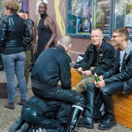 Skinhead sitting in a company of his friends while using his partner as a stool to sit on, at Folsom Europe Street Fair, the biggest European gay fetish event, in Berlin, Germany, photo by Ivan Kralj