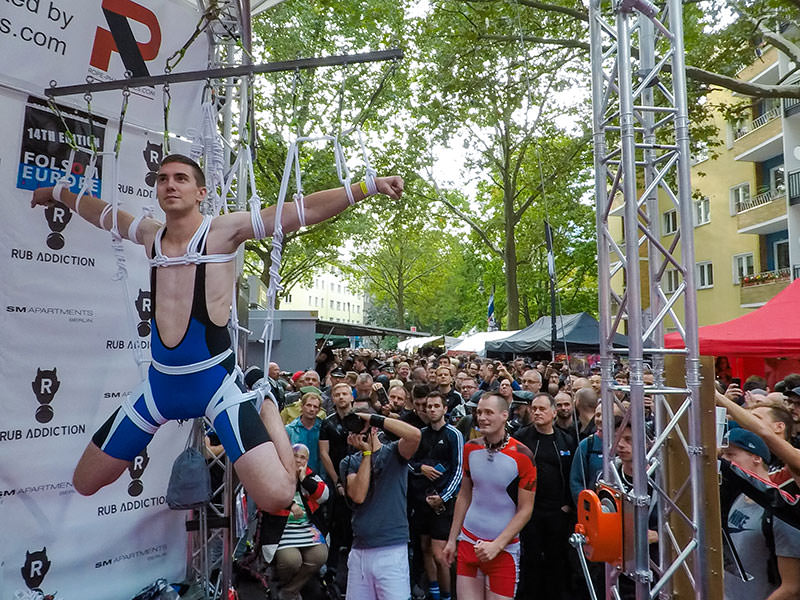 People watching the shibari performance, a man tied in shibari style, hanging at Folsom Europe Street Fair, the biggest European gay fetish event, in Berlin, Germany, photo by Ivan Kralj