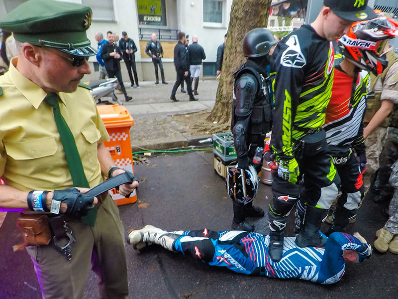 A biker is standing on chests of another one, while the man dressed as a policeman observes, at Folsom Europe Street Fair, the biggest European gay fetish event, in Berlin, Germany, photo by Ivan Kralj