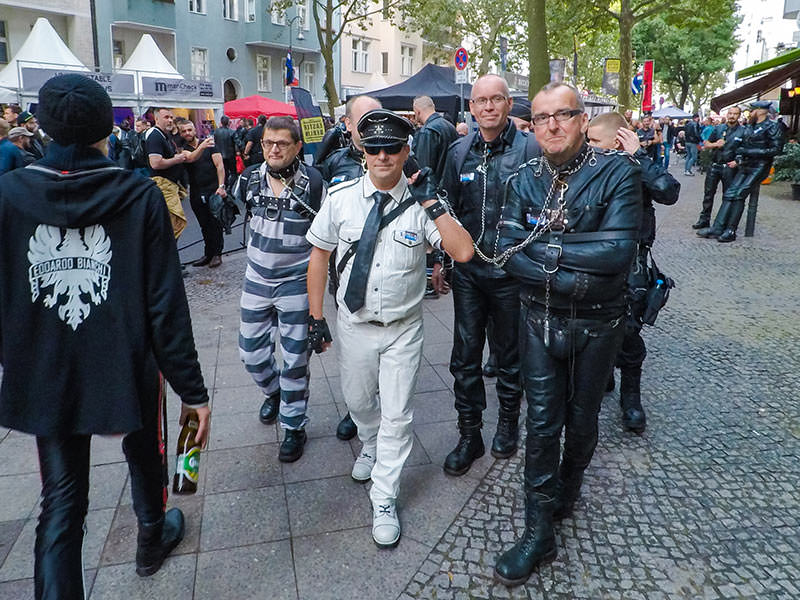 A man dressed in uniform is leading prisoners-looking men in chains at Folsom Europe Street Fair, the biggest European gay fetish event, in Berlin, Germany, photo by Ivan Kralj