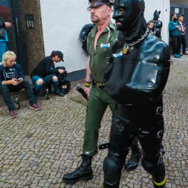 Man constrained in latex being escorted by a military-looking official at Folsom Europe Street Fair, the biggest European gay fetish event, in Berlin, Germany, photo by Ivan Kralj