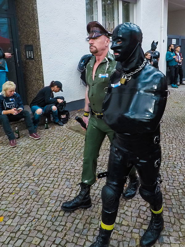 Man constrained in latex being escorted by a military-looking official at Folsom Europe Street Fair, the biggest European gay fetish event, in Berlin, Germany, photo by Ivan Kralj