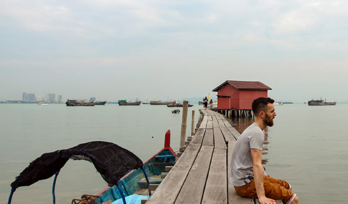 Pipeaway blogger Ivan Kralj sitting on one of the jetties in Georgetown, Penang Island, Malaysia, boats lining up on the horizon, photo by Weile Ng