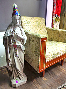 Statue of Jesus Christ with a birthday hat on his head and holding the cross with a sign "Miracles happen" placed next to a retro armchair in Romanian Kitsch Museum, in Bucharest, Romania, photo by Ivan Kralj.