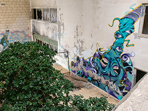 An atrium in the abandoned Hotel Belvedere Dubrovnik, Croatia, with a growing tree and large street art mural on the wall, photo by Ivan Kralj