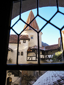 Bran Castle (also known as Dracula Castle) red-tile covered tower shot through the grid window, photo by Ivan Kralj