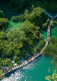 Visitors of Plitvice Lakes national park in Croatia walking over a wooden pathway over green lakes, from bird's eye perspective, photo by Ivan Kralj