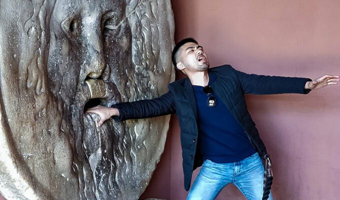 Tourist places his hand into Bocca della Verita, Mouth of Truth, and pretends the sculpture is biting it off for the camera, Basilica of Santa Maria in Cosmedin, Rome, Italy, photo by Ivan Kralj