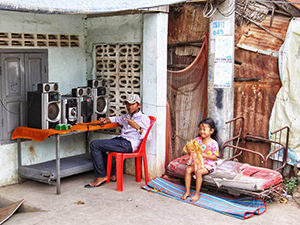 Cambodian boy sitting next to the sound system installed on the table in front of his house, while his sister plays with a doll, in Battambang, during the Khmer New Year, photo by Ivan Kralj